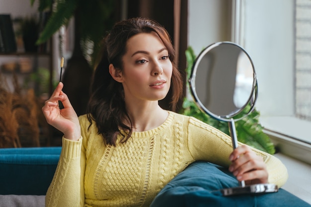 Jeune jolie femme se maquille à la maison tout en regardant dans le miroir