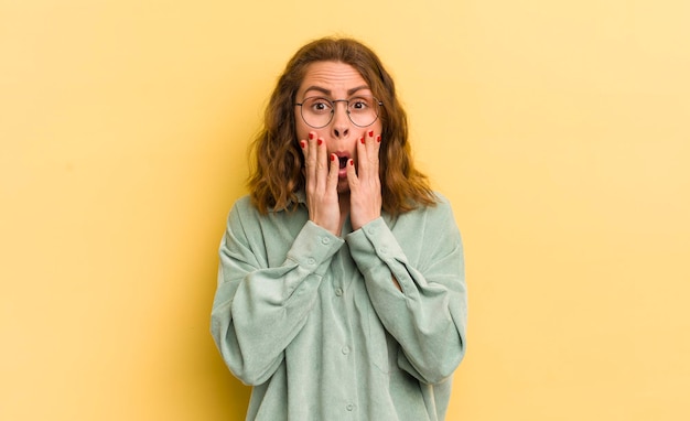 Jeune jolie femme se sentant choquée et effrayée, terrifiée avec la bouche ouverte et les mains sur les joues