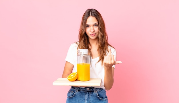 Jeune jolie femme se sentant en colère, agacée, rebelle et agressive et tenant un plateau avec un jus d'orange