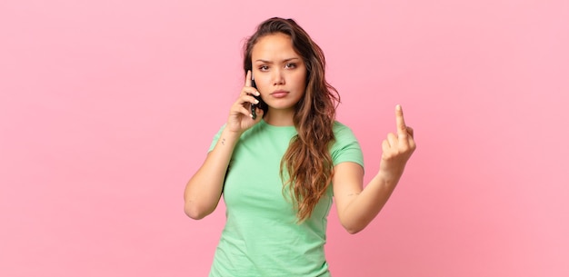 Jeune jolie femme se sentant en colère, agacée, rebelle et agressive et tenant un téléphone intelligent