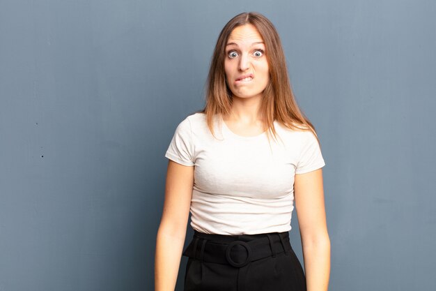 Jeune jolie femme se sentant désemparée, confuse et incertaine quant à l'option à choisir, essayant de résoudre le problème contre le mur gris