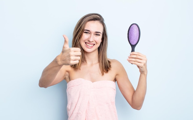 Jeune jolie femme se sentant fière de sourire positivement avec le concept de brosse à cheveux pouce en l'air