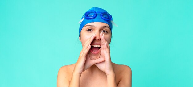 Jeune jolie femme se sentant heureuse, donnant un grand cri avec les mains à côté de la bouche avec des lunettes de natation