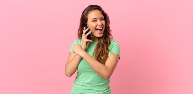 Jeune jolie femme se sentant heureuse et faisant face à un défi ou célébrant et tenant un téléphone intelligent