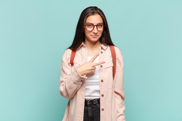 Jeune jolie femme se sentant heureuse, positive et réussie, avec la main en forme de v sur la poitrine, montrant la victoire ou la paix