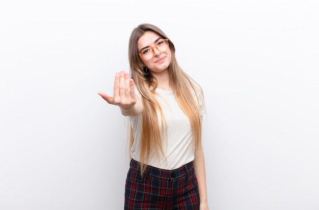 Jeune jolie femme se sentant heureuse, réussie et confiante, face à un défi et disant: lancez-le! ou vous accueillir contre un mur blanc