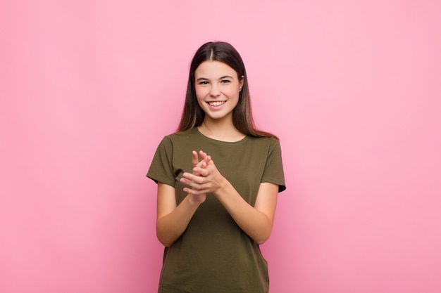 Jeune jolie femme se sentant heureuse et réussie, souriant et applaudissant, disant félicitations avec des applaudissements contre le mur rose