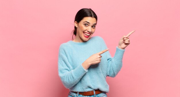 Jeune jolie femme se sentant joyeuse et surprise, souriante avec une expression choquée et pointant vers le côté