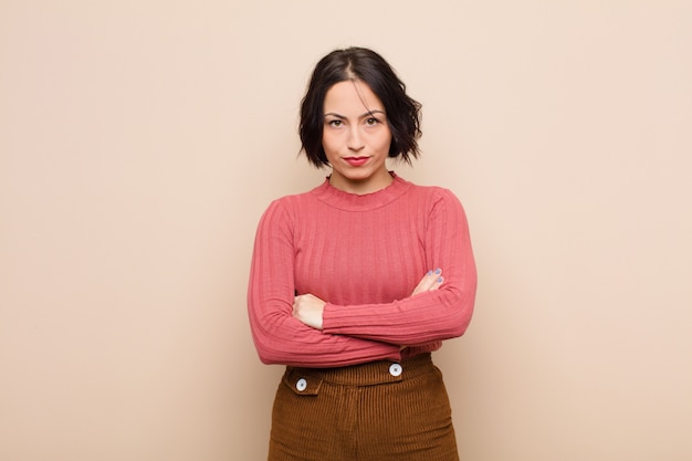 Jeune jolie femme se sentant mécontente et déçue, l'air sérieuse, agacée et en colère avec les bras croisés contre le mur beige