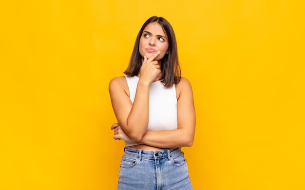 Jeune jolie femme se sentant réfléchie, se demandant ou imaginant des idées, rêvassant et levant pour copier l'espace