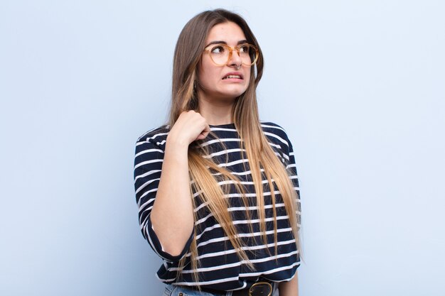 Jeune jolie femme se sentant stressée, anxieuse, fatiguée et frustrée, tirant le cou de la chemise, frustrée par le problème contre le mur bleu doux