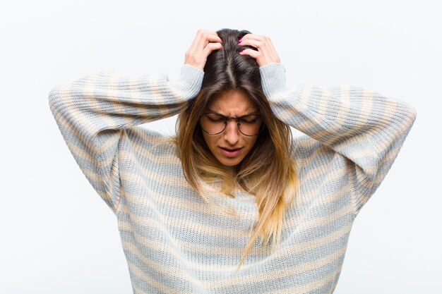 Jeune jolie femme se sentant stressée et frustrée, levant les mains à la tête, se sentant fatiguée, malheureuse et souffrant de migraine sur un mur blanc