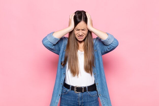 Jeune jolie femme se sentant stressée et frustrée, levant les mains à la tête, se sentant fatiguée, malheureuse et souffrant de migraine