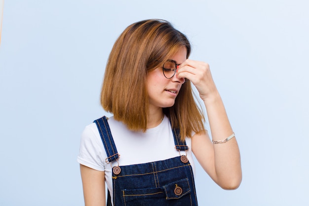 Jeune jolie femme se sentant stressée, malheureuse et frustrée, touchant le front et souffrant de migraine de maux de tête sévères sur fond bleu