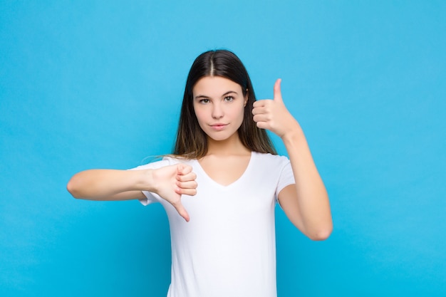 Jeune jolie femme se sentir confus, désemparé et incertain, pondérant le bien et le mal dans différentes options ou choix contre le mur bleu