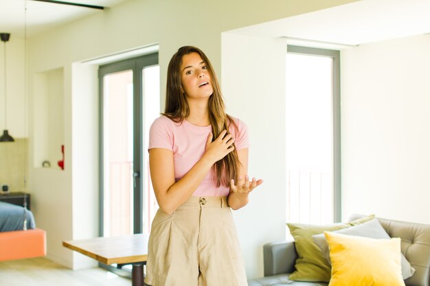 Jeune jolie femme se sentir heureuse et amoureuse, souriant d'une main à côté du cœur et de l'autre tendue à l'avant