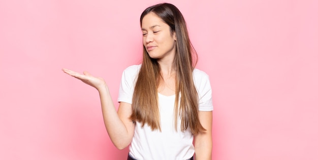 Jeune jolie femme se sentir heureuse et souriante avec désinvolture, à la recherche d'un objet ou d'un concept tenu sur la main sur le côté