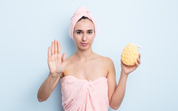 Jeune jolie femme semblant sérieuse montrant la paume ouverte faisant un geste d'arrêt. concept de douche et éponge