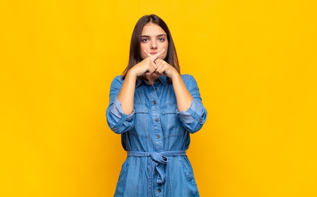 Jeune jolie femme à la sérieuse et mécontente avec les deux doigts croisés à l'avant dans le rejet, demandant le silence