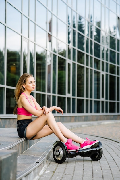 Jeune jolie femme en short et haut assis avec hoverboard dans la rue
