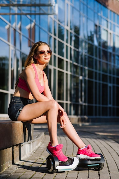 Jeune jolie femme en short et haut assis avec hoverboard dans la rue