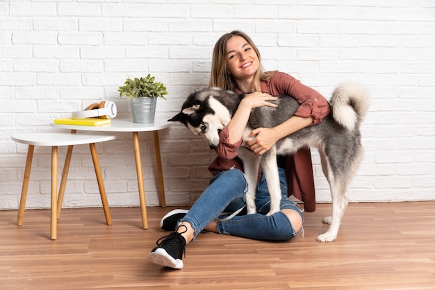 Jeune jolie femme avec son chien husky assis sur le sol à l'intérieur