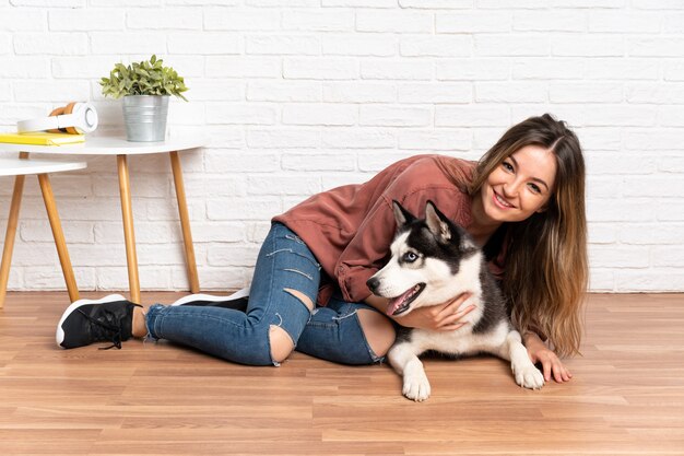 Jeune jolie femme avec son chien husky assis sur le sol à l'intérieur