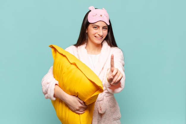 Jeune jolie femme souriant fièrement et en toute confiance faisant la pose numéro un triomphalement, se sentant comme un leader. réveil portant le concept de pyjama