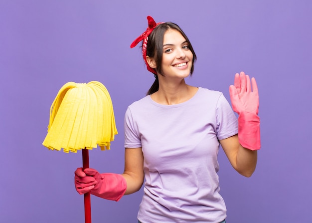 Jeune jolie femme souriant joyeusement et gaiement, agitant la main, vous accueillant et vous saluant, ou vous disant au revoir