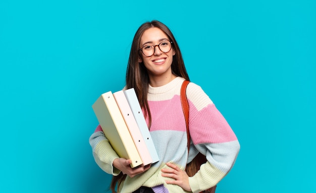 Jeune jolie femme souriant joyeusement avec une main sur la hanche et une attitude confiante, positive, fière et amicale