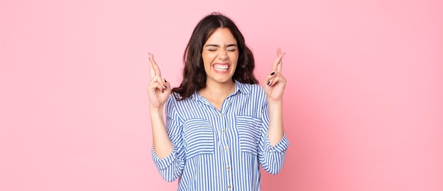 Jeune jolie femme souriante et croisant anxieusement les deux doigts, se sentant inquiète et souhaitant ou espérant bonne chance