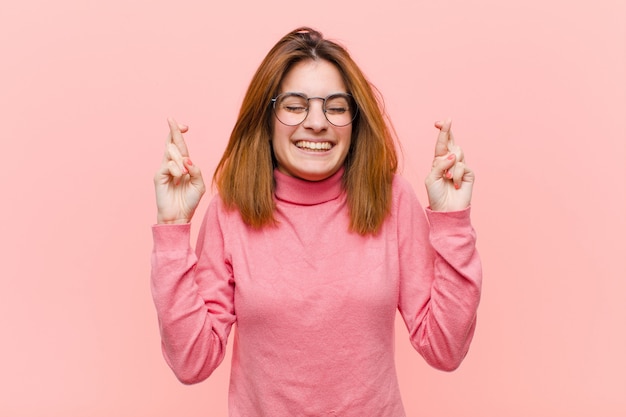 Jeune jolie femme souriante et croisant anxieusement les deux doigts, se sentant inquiète et souhaitant ou espérant bonne chance