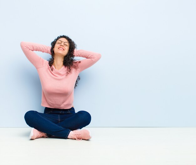 Jeune jolie femme souriante et détendue, satisfaite et insouciante, riant positivement et se reposant assis sur le sol