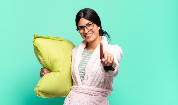 Jeune jolie femme souriante fièrement et avec confiance faisant triomphalement la pose numéro un, se sentant comme un leader. concept de pyjama