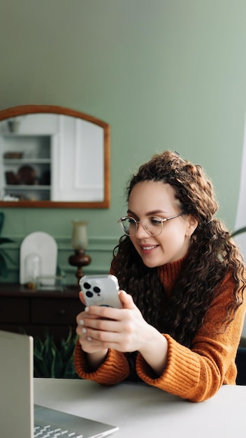 Jeune jolie femme souriante heureuse assise à table tenant un smartphone à l'aide d'un téléphone portable moderne