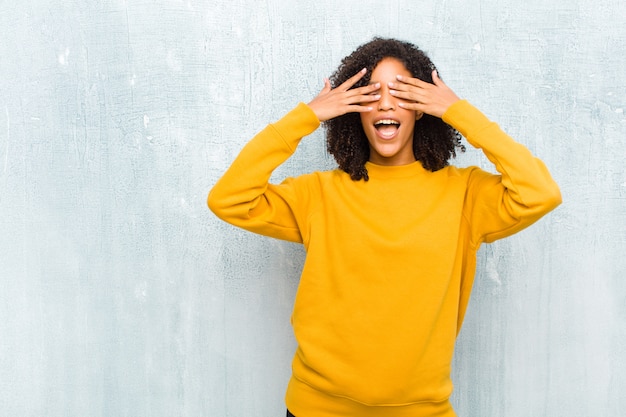 Jeune jolie femme souriante et heureuse, couvrant les yeux des deux mains et attendant une surprise incroyable