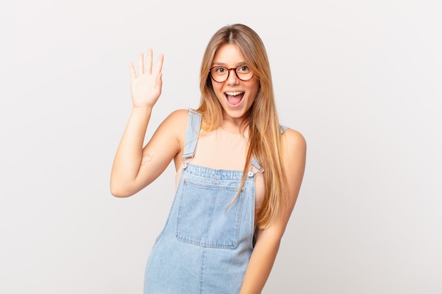 Jeune jolie femme souriante joyeusement, agitant la main, vous accueillant et vous saluant