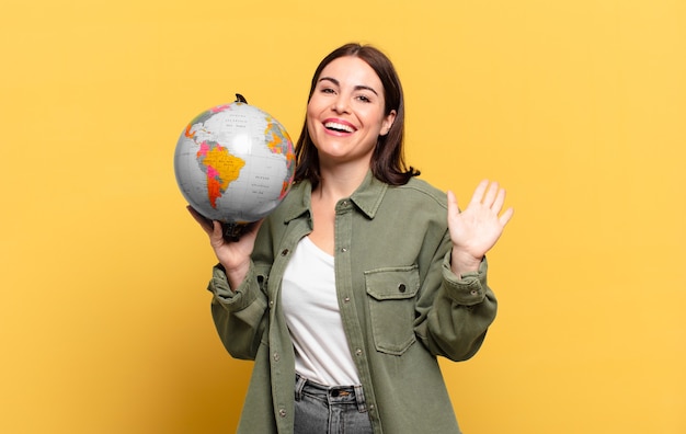 Jeune jolie femme souriante joyeusement et joyeusement, agitant la main, vous accueillant et vous saluant, ou vous disant au revoir