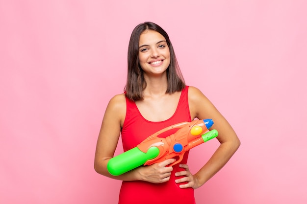 Jeune jolie femme souriante joyeusement avec une main sur la hanche et une attitude confiante, positive, fière et amicale