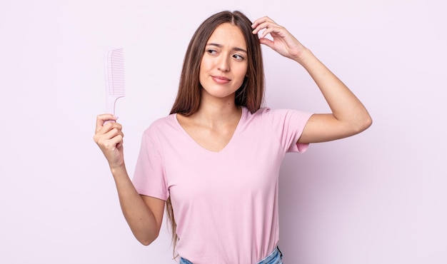 Jeune jolie femme souriante joyeusement et rêvant ou doutant. concept de peigne à cheveux