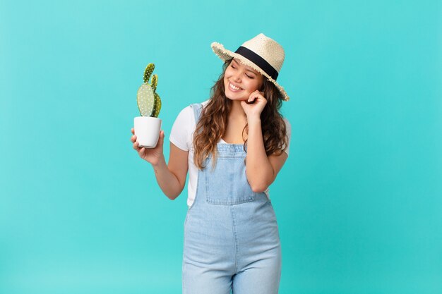 jeune jolie femme souriante joyeusement et rêvant ou doutant et tenant un cactus