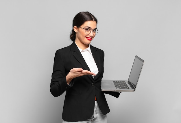 Jeune jolie femme souriante joyeusement, se sentant heureuse et montrant un concept dans l'espace de copie avec la paume de la main. concept d'ordinateur portable