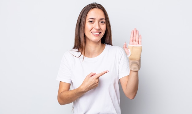 Jeune jolie femme souriante joyeusement, se sentant heureuse et pointant sur le côté. concept de bandage à la main