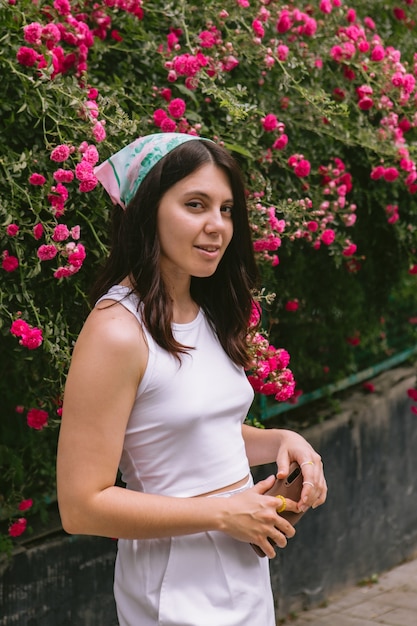 Jeune jolie femme souriante près de l'espace de copie de buisson de roses rouges en fleurs