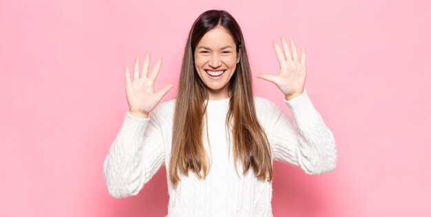 Jeune jolie femme souriante et à la recherche amicale, montrant le numéro dix ou dixième avec la main en avant, compte à rebours