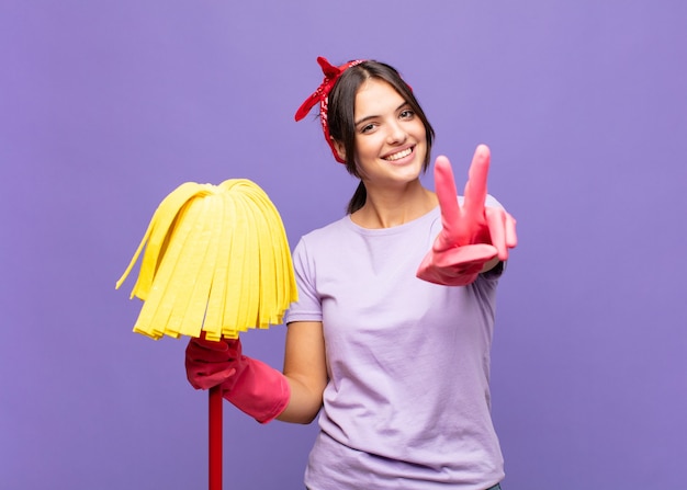 Jeune jolie femme souriante et à la recherche heureuse, insouciante et positive, gesticulant la victoire ou la paix d'une seule main