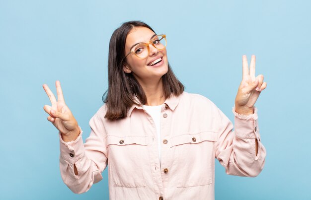 Jeune jolie femme souriante et à la recherche heureuse, sympathique et satisfaite, gesticulant la victoire ou la paix à deux mains