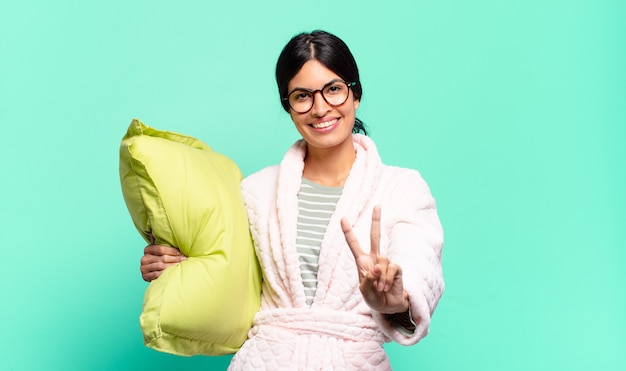 Jeune jolie femme souriante et semblant heureuse, insouciante et positive, gesticulant la victoire ou la paix d'une main. concept de pyjama