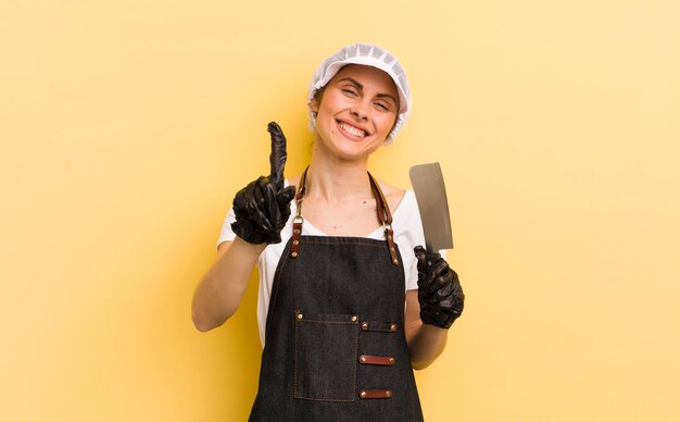 Jeune jolie femme souriante et sympathique montrant le concept de boucher numéro un