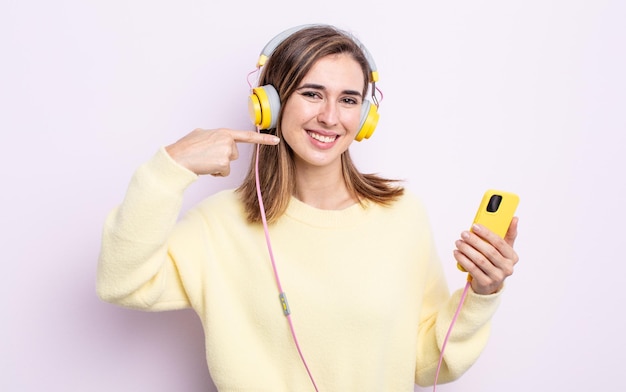 Jeune jolie femme souriante en toute confiance pointant vers son large sourire. casque et concept de téléphone